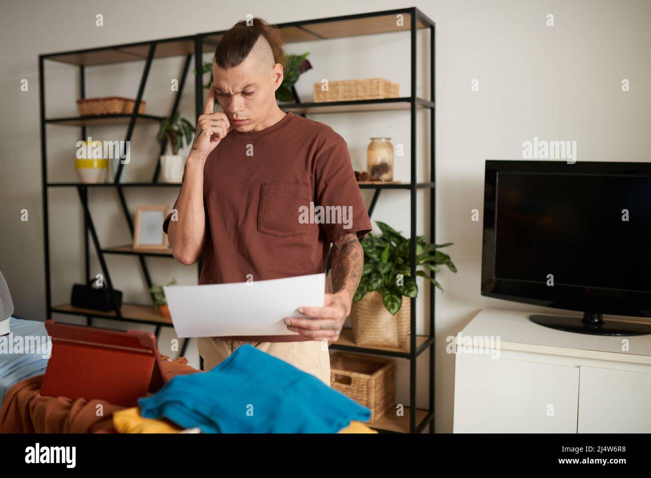 Confused young man standing at ironing board in his apartment and ...