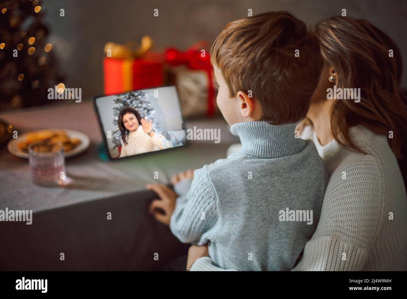 Happy young woman with little son, talking with friends on virtual zoom video call, celebrating new year party in holiday remote online conference cha Stock Photo