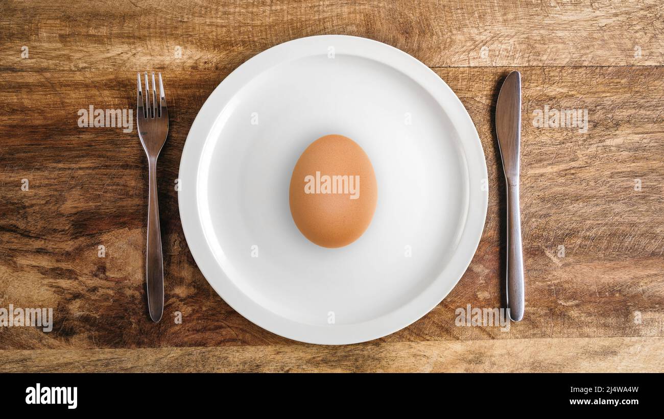 Raw egg on white plate against wooden table with knife and fork, top view Stock Photo