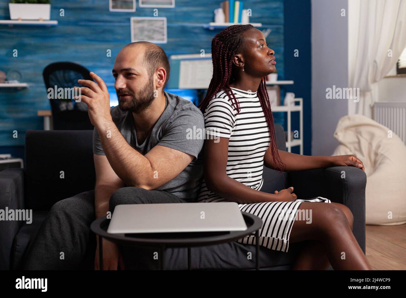 Caucasian man confronting african american woman about financial and banking issues. Emotive young adult couple arguing about serious marriage problems while sitting on sofa at home Stock Photo