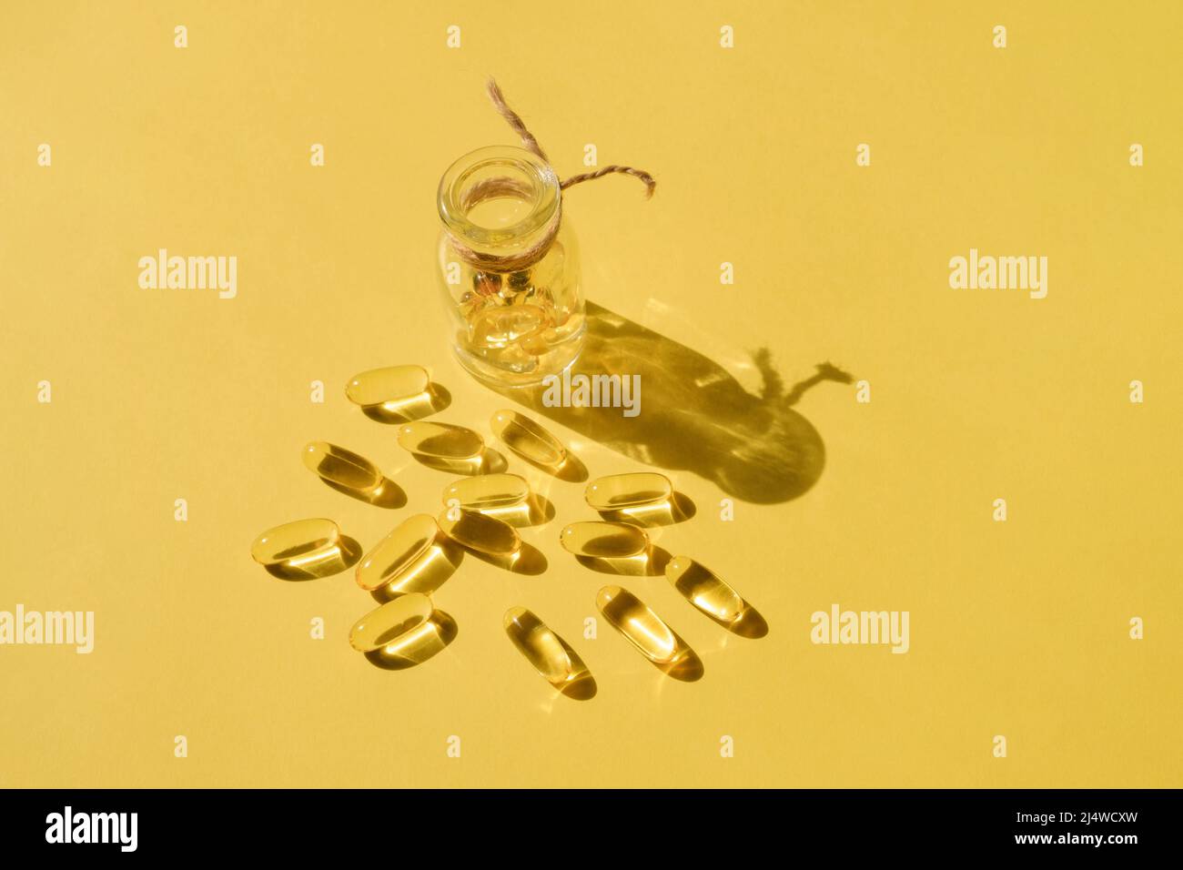 Pills and glass pill bottle on yellow background. Big golden tablets. Omega 3 capsules. Close up, top view. Health care concept. Healthy every day Stock Photo