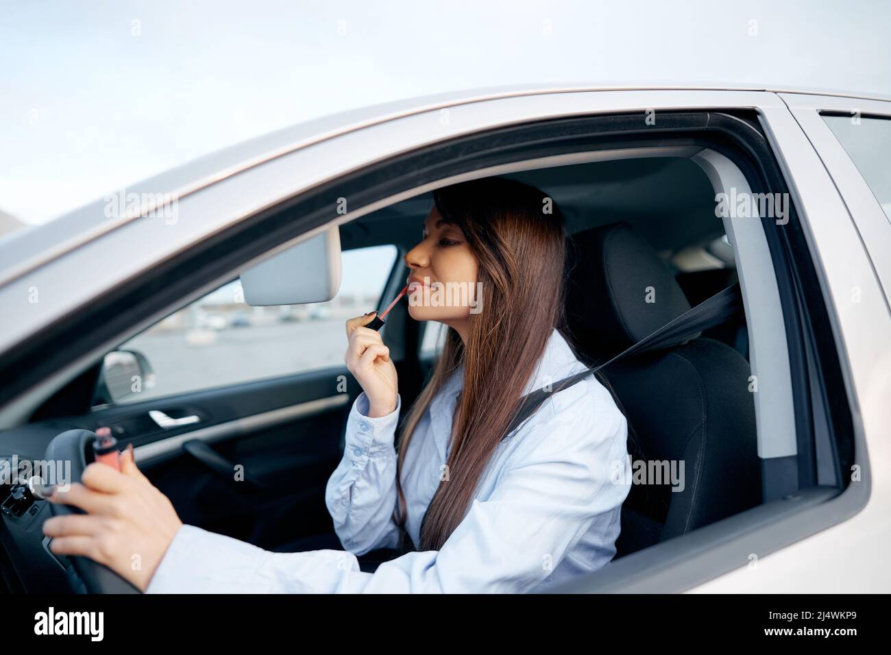 beautiful woman doing makeup in the car and looking in a mirror driving car. Stock Photo