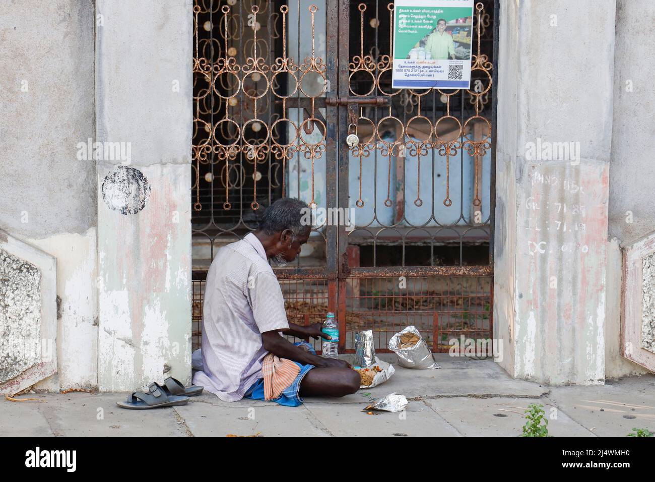 Man sitting in the doorway of a dilapidated house eating his lunch in Trichy, Tamil Nadu, India Stock Photo