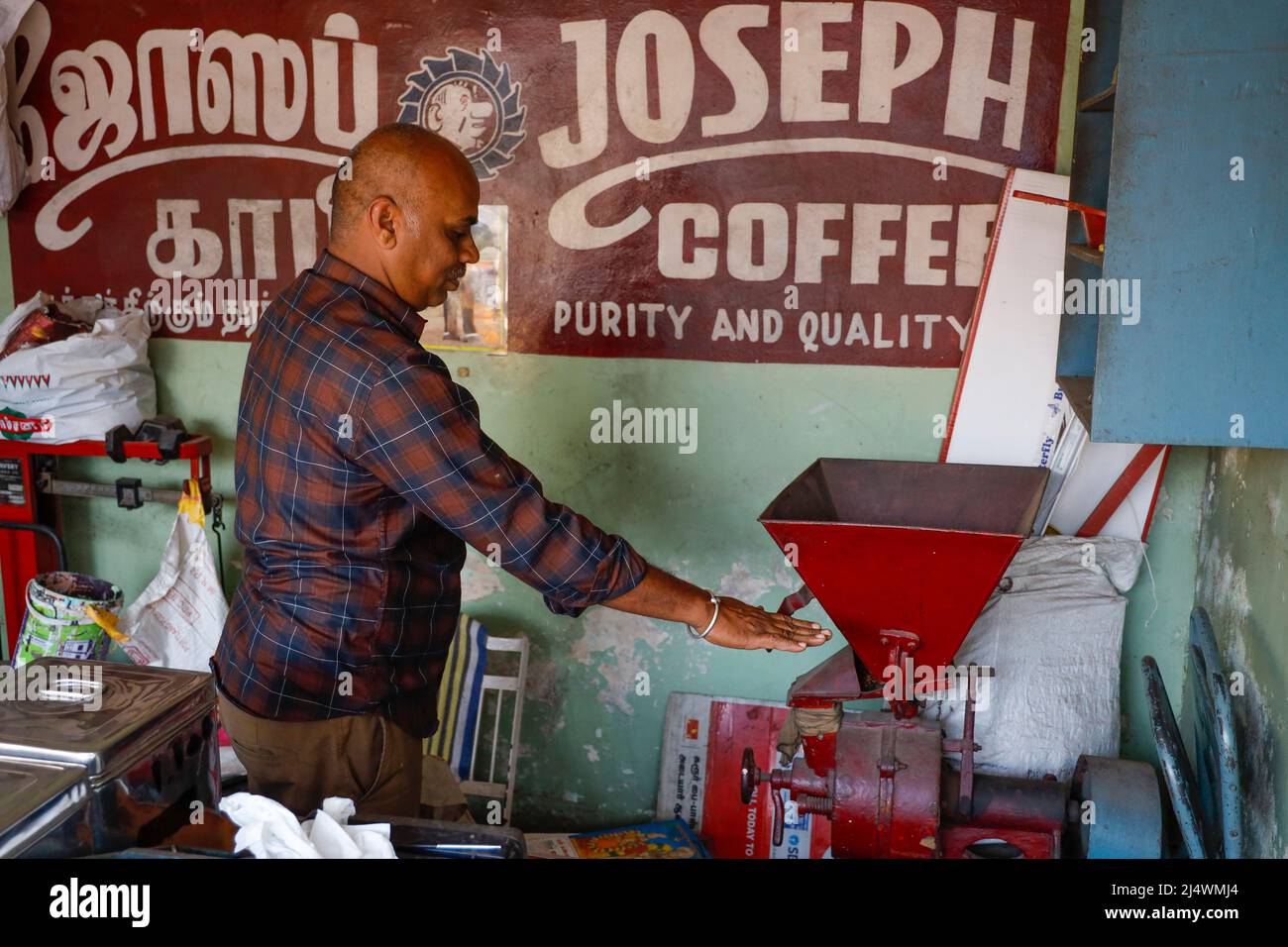 Coffee salesman working the grinder in his shop in Trichy, Tamil Nadu