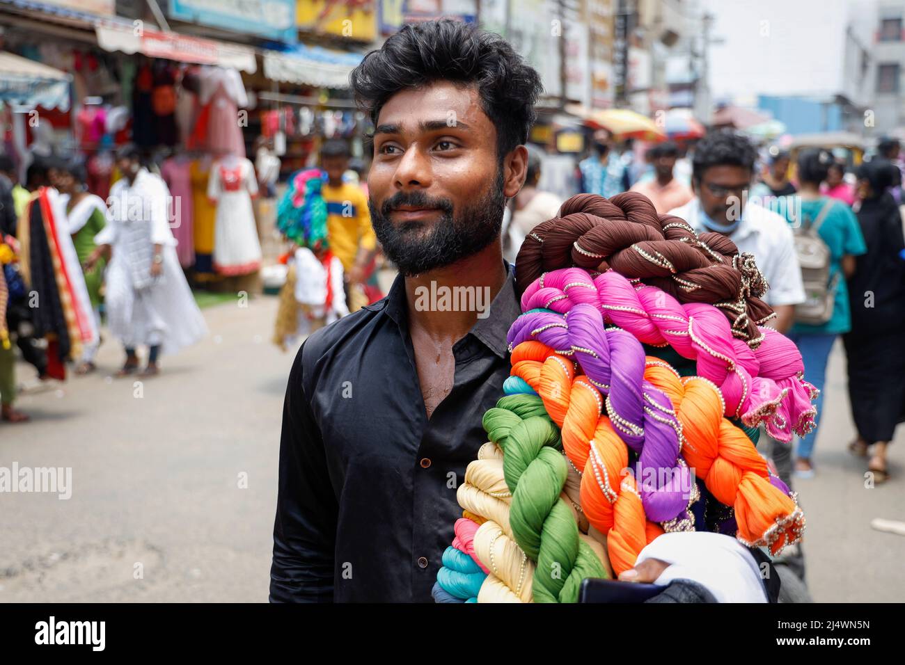 Young male street vendor carrying colourful shawls on his shoulder in a street in Trichy, Tamil Nadu, India Stock Photo