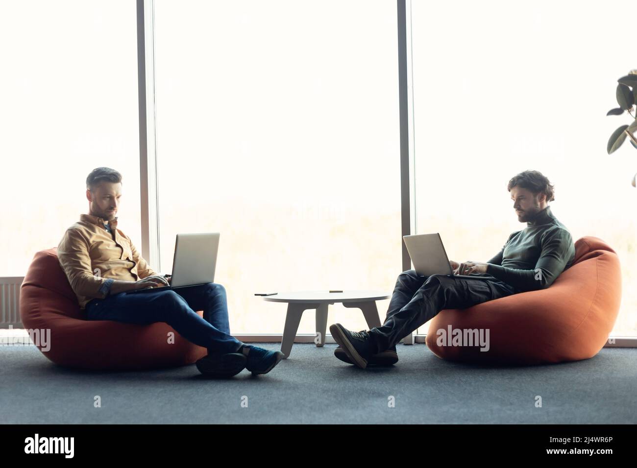 Focused colleagues sitting in bean bag chairs, working with laptop