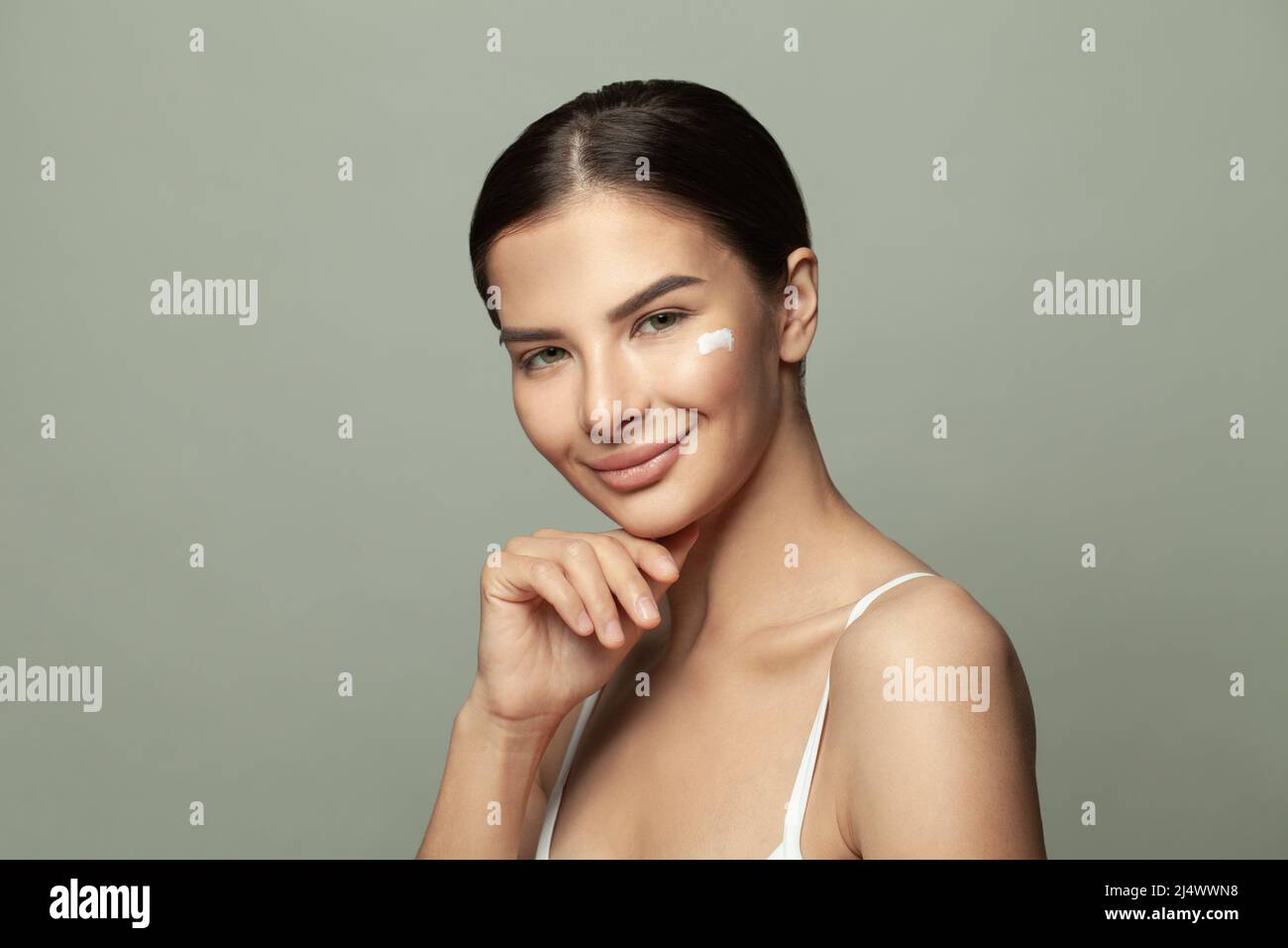 Cheerful beautiful woman applies cream on her face, beauty treatments cares about skin Stock Photo