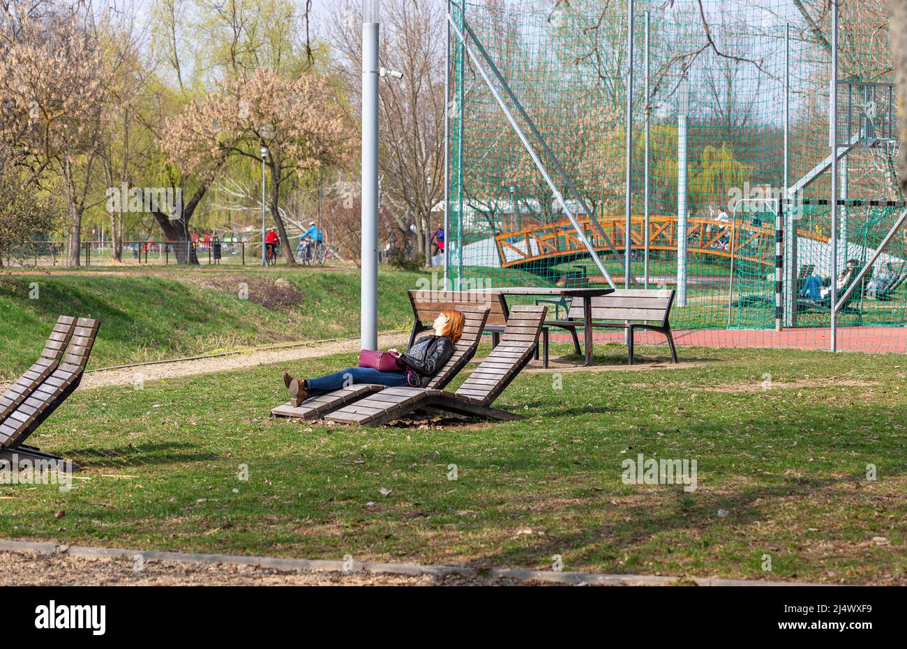Nyiregyhaza, Hungary – March 24, 2019: Salt Lake (Sosto) Park. Wooden outdoor furniture, football field, red-haired girl resting on wooden sun lounger Stock Photo