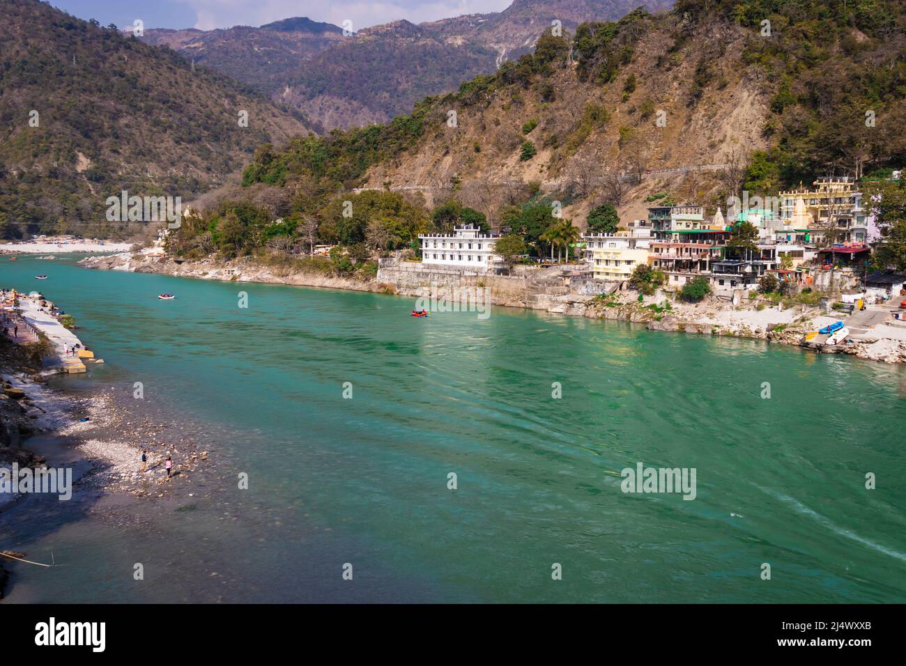 ganges river flowing through mountains with city nestled at riverbank from top angle image is taken at rishikesh uttrakhand india on Mar 15 2022. Stock Photo
