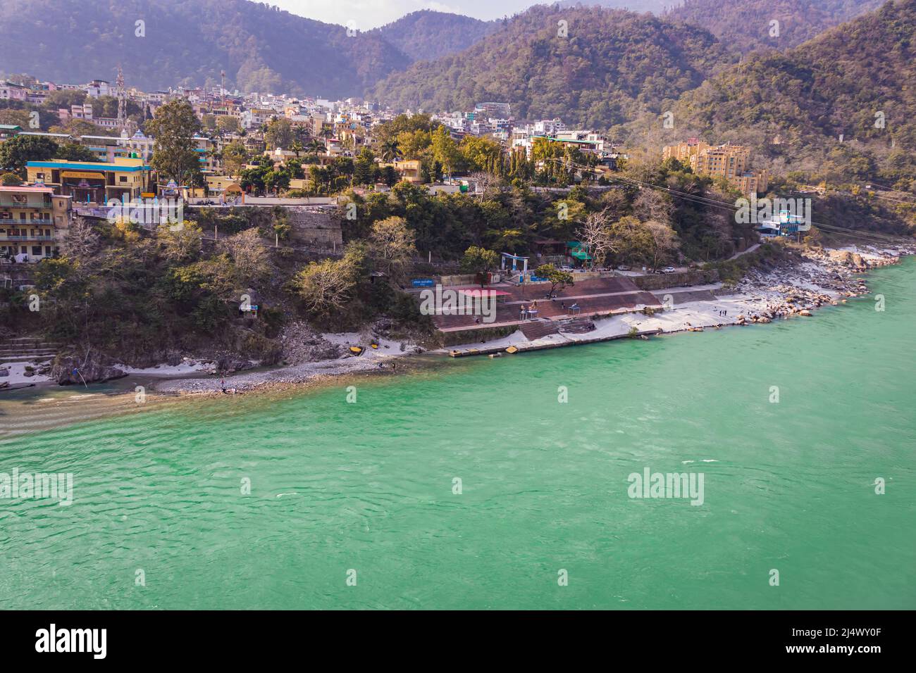 ganges river flowing through mountains with city nestled at riverbank from top angle image is taken at rishikesh uttrakhand india on Mar 15 2022. Stock Photo