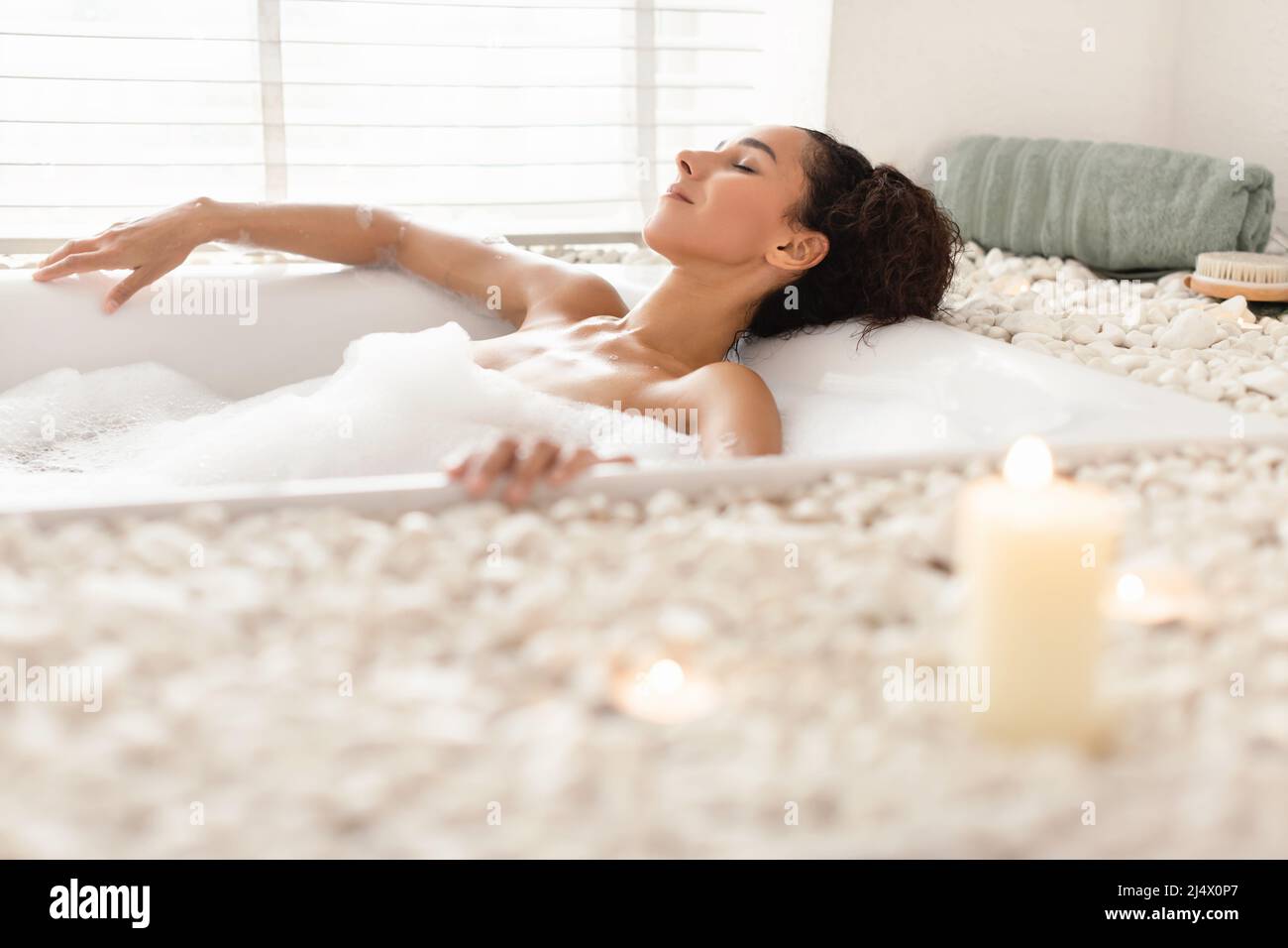 Lovely young woman lying in foamy bath in relaxing atmosphere with candles at home, free space Stock Photo