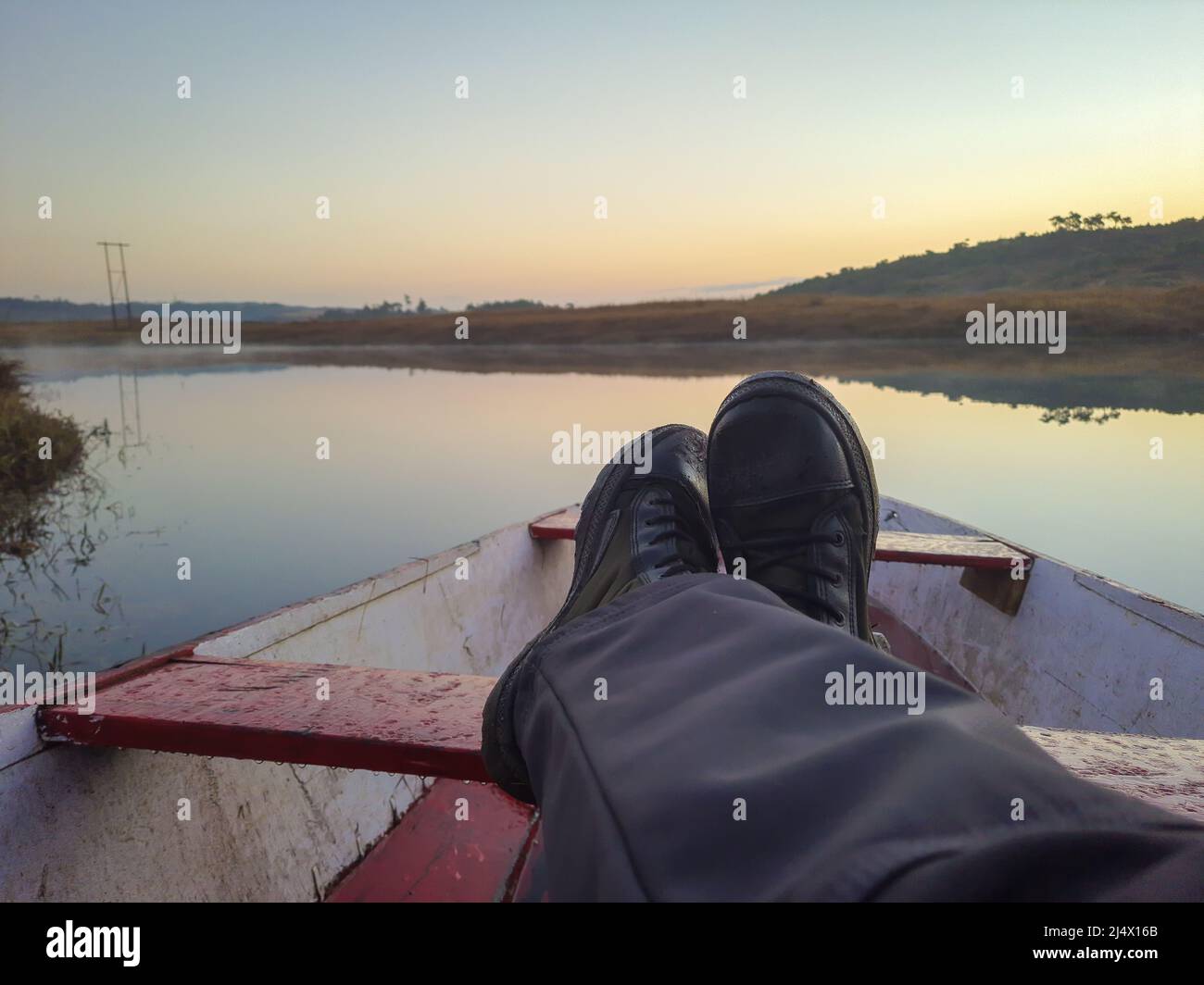 man foot on traditional wood boat at calm lake with dramatic sunrise ...