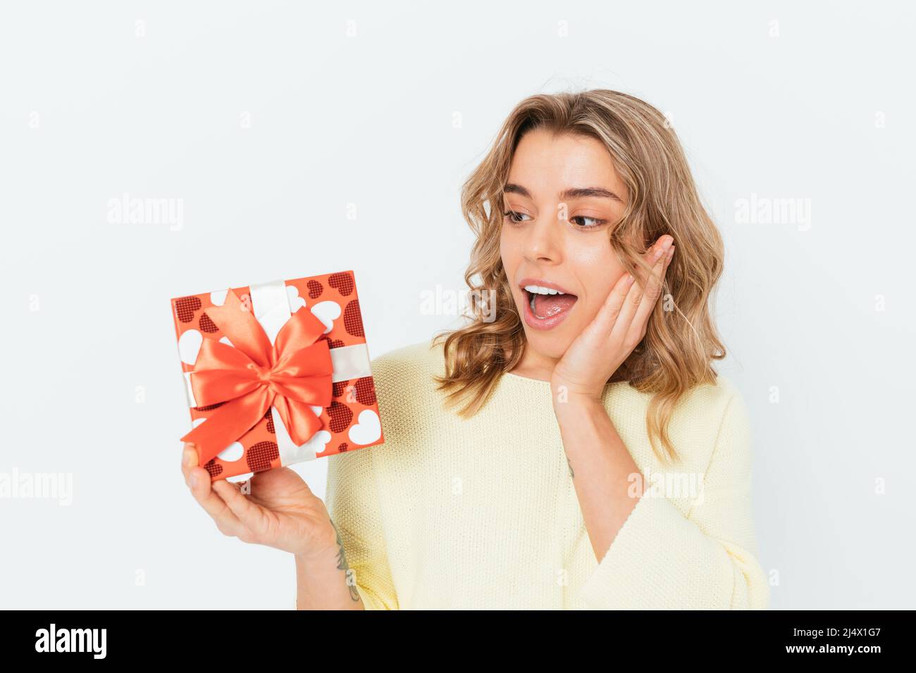 Surprised happy blonde girl holding a red gift box in her hand can't ...