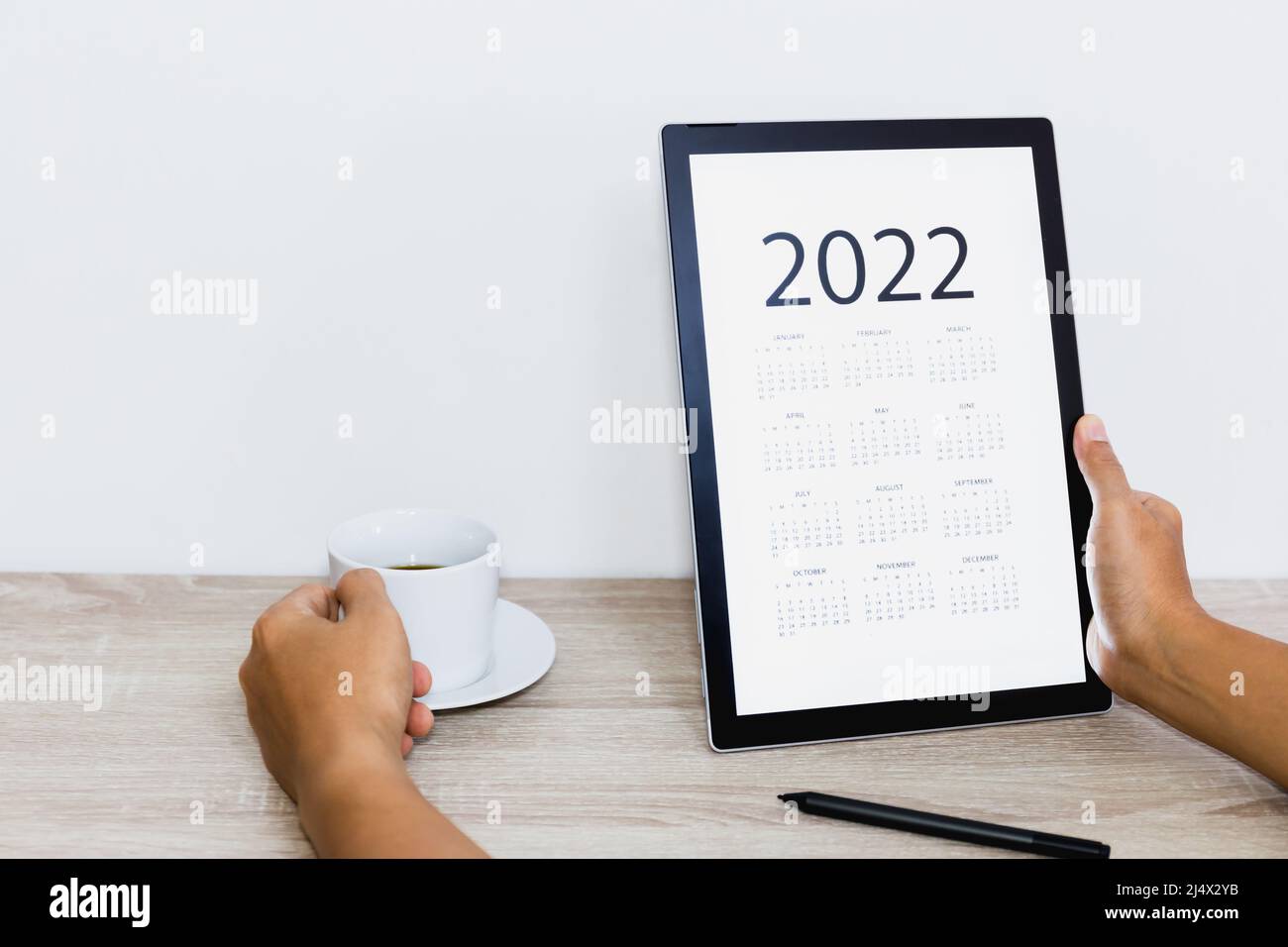 Hand holding coffee cup while looking calendar on digital tablet. Stock Photo