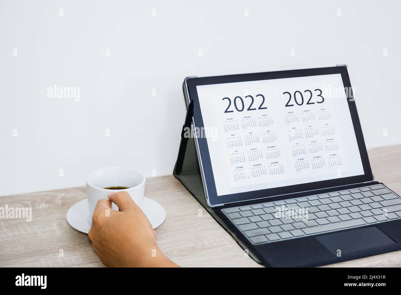 Hand holding coffee cup while looking calendar on digital tablet. Stock Photo