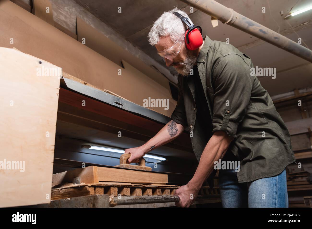 woodworker in earmuffs polishing timber in sander machine Stock Photo