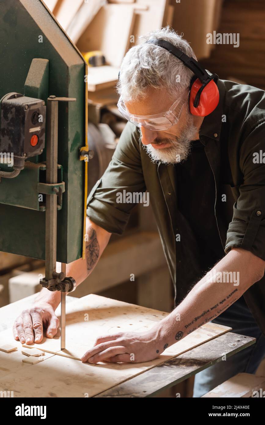 bearded woodworker in goggles cutting plank on band saw Stock Photo Alamy