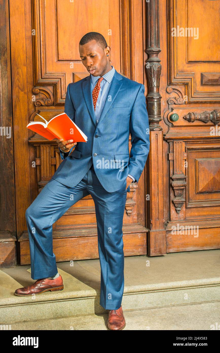 Dressing formally in blue suit, patterned shirt, necktie, short haircut, wearing ear stud, a young black teacher is standing in the front of old style Stock Photo