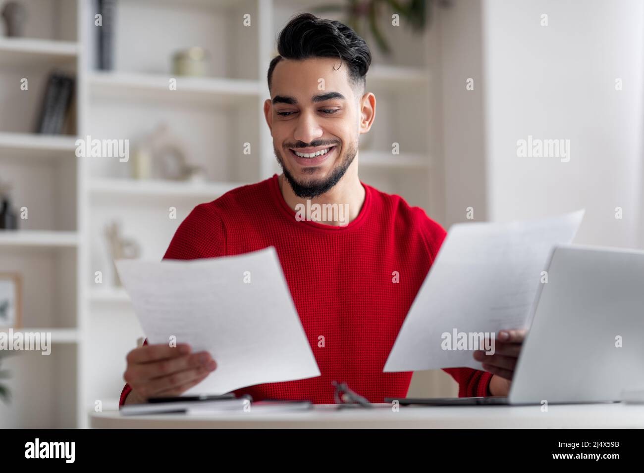 Cheerful attractive millennial muslim businessman analyst manager with beard works with documents, papers at workplace Stock Photo