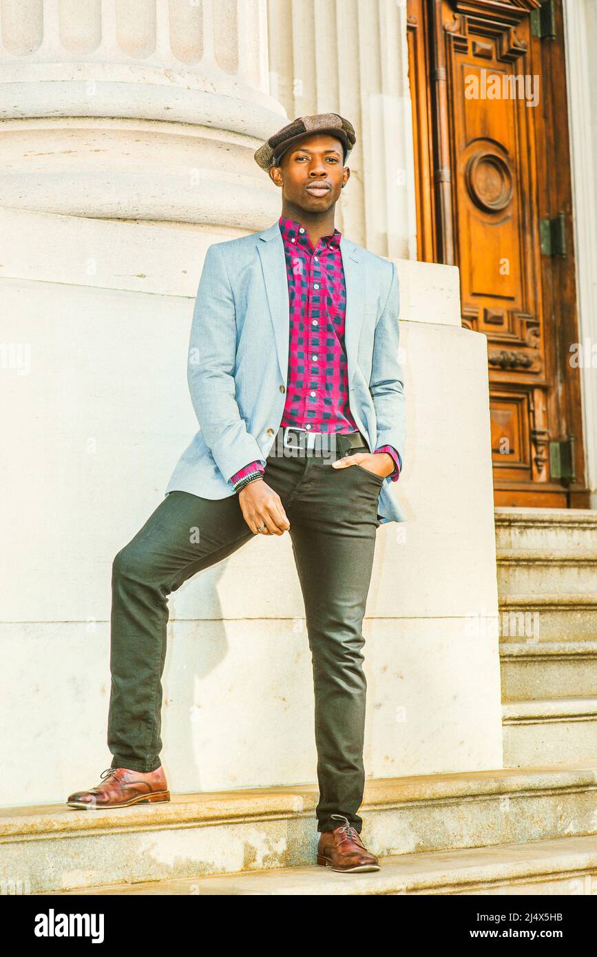 Man Urban Fashion. Wearing fashionable newsboy cap, dressing in light gray blazer, patterned pink, black under shirt, black pants, brown leather shoes Stock Photo