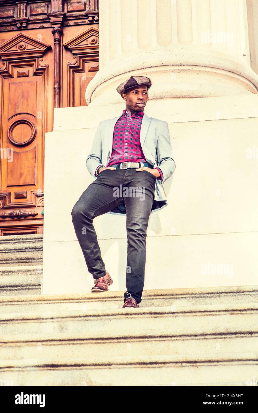 Urban fashion. Wearing newsboy cap, dressing in blazer, patterned under shirt, pants, leather shoes, a young black guy standing stairs outside vintage Stock Photo