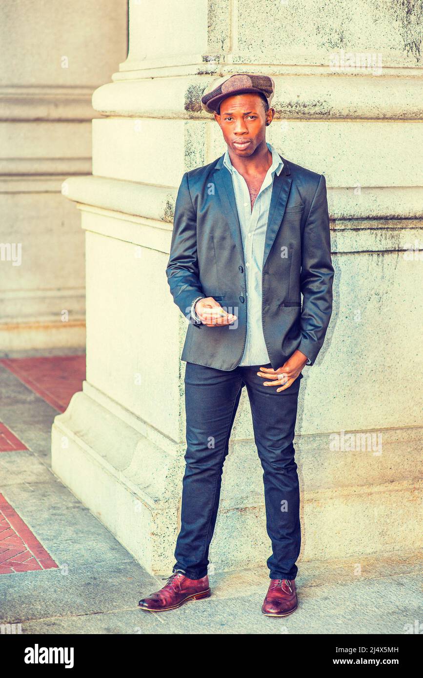 Wearing fashionable Newsboy cap, dressing in black blazer, pants, brown  leather shoes, a young black guy standing by column on street, holding a  mobil Stock Photo - Alamy