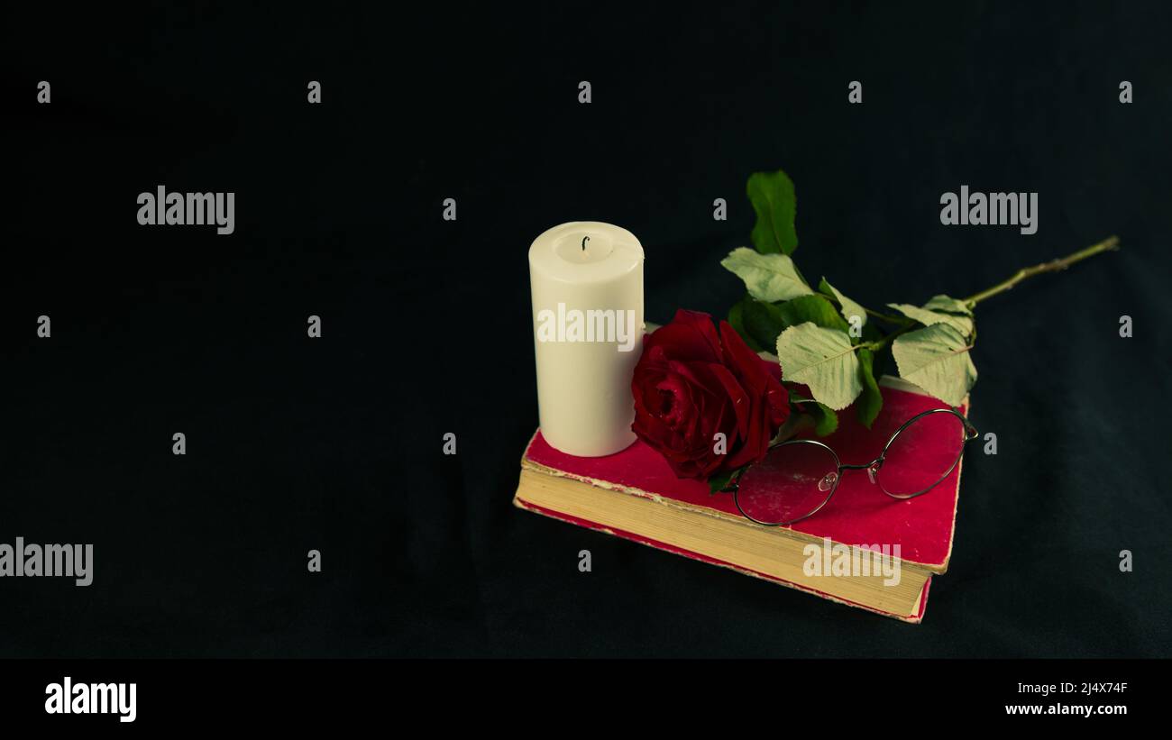 Big white candle, red rose, glasses on old book. Romantic composition ...