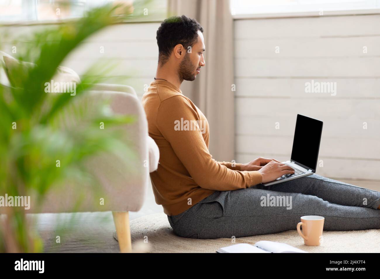 Arab man using laptop sitting on floor at home Stock Photo
