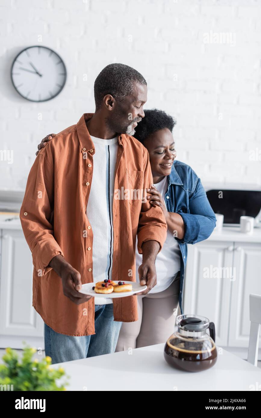 happy african american woman hugging husband holding pancakes in ...