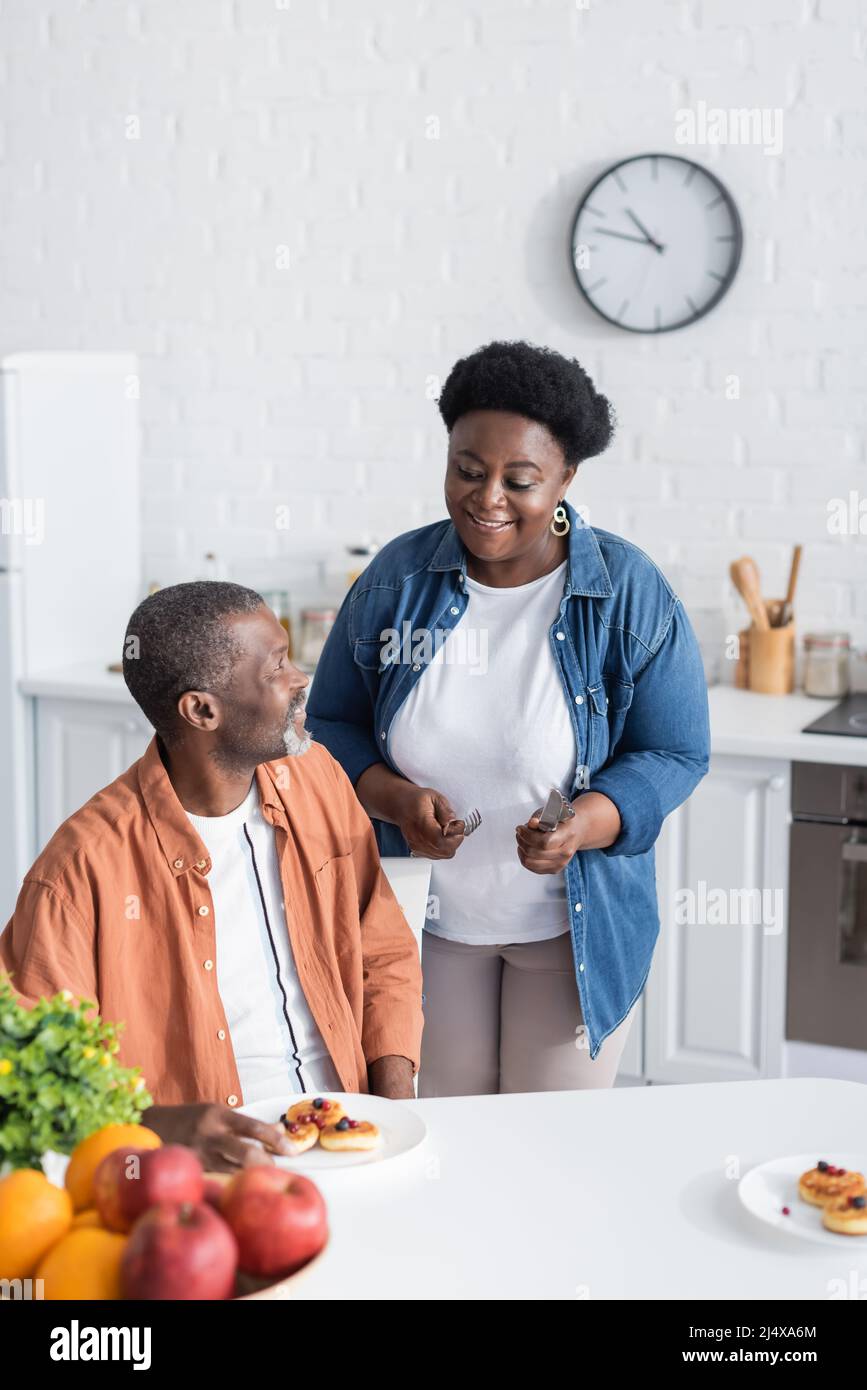 happy and senior african american woman holding cutlery near husband ...