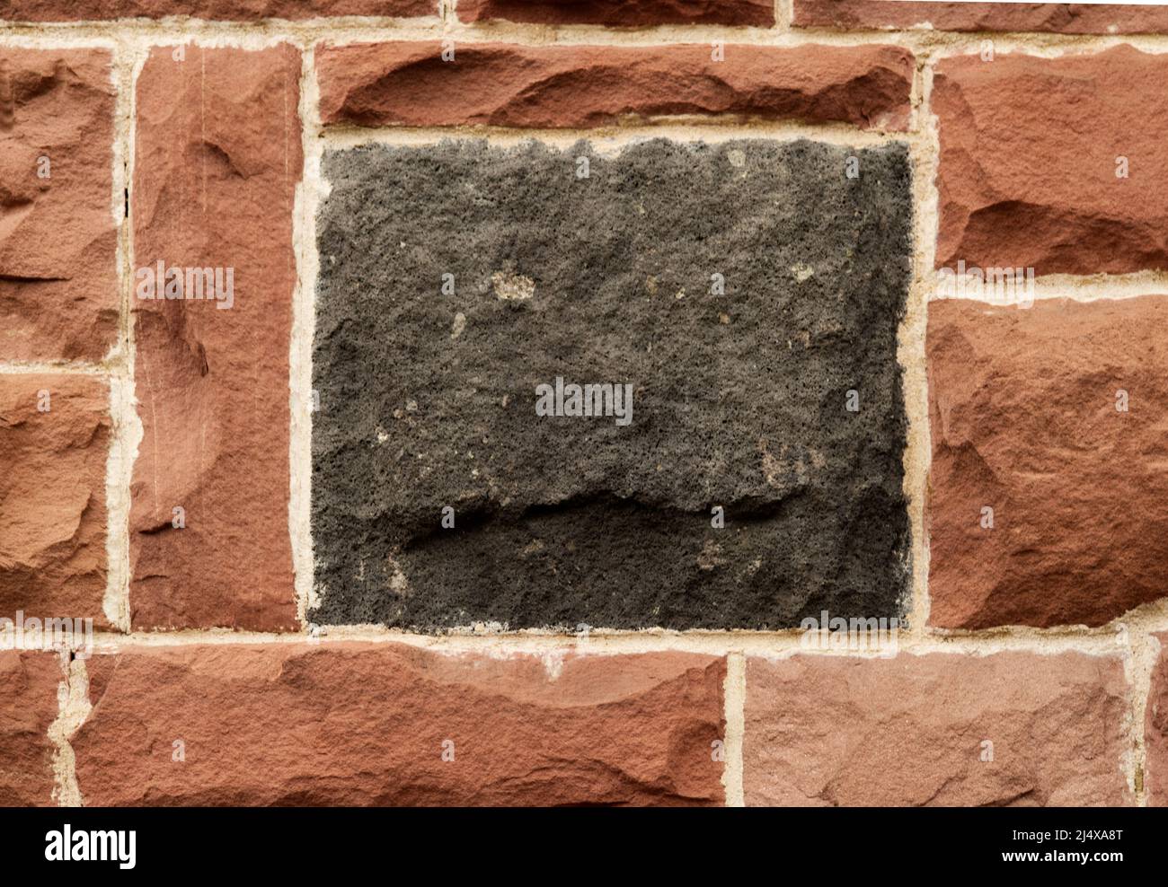 Stone wall with single black square stone in the center and several red stones in orderly pattern around it Stock Photo