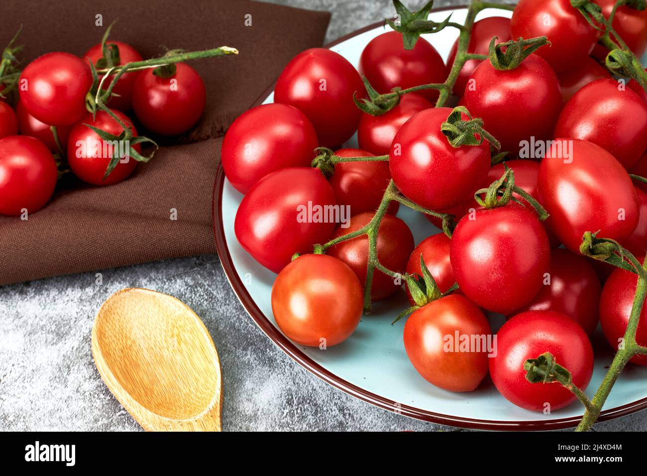 Composition of ripe cherry tomatoes on a plate and a wooden spoon on a stone countertop. Healthy food. Vegan food. Vegetarian food Stock Photo