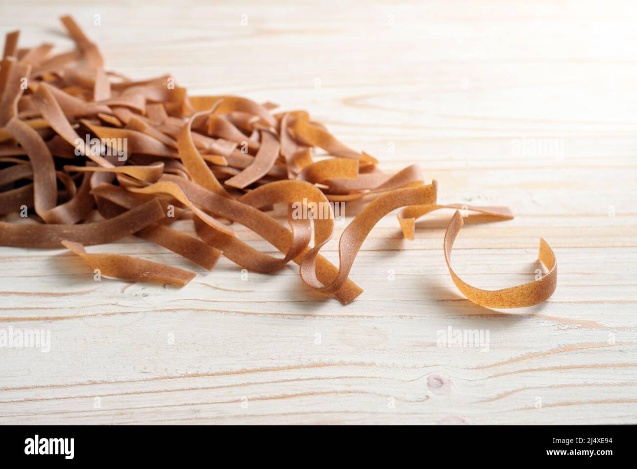 Heap of wholegrain tagliatelle noodles, healthy pasta alternative with fiber, protein, B vitamins and minerals, light wooden table, copy space, select Stock Photo