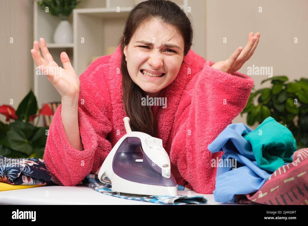 A housewife in a pink robe is hard to iron clothes with a bad iron