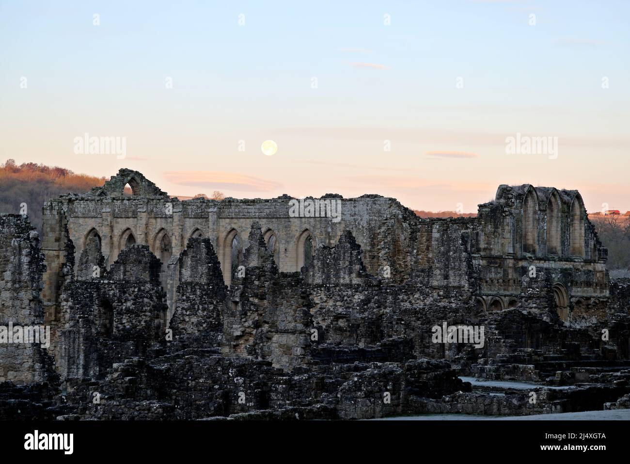 The wall of the warming house behind which is the refectory of ruined Rievaulx Cistercian Abbey at sunrise & after the moon has risen Stock Photo