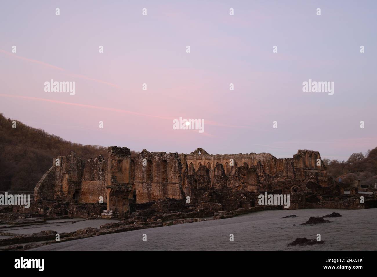Infirmary cloister wall: cloister behind, & ruins foreground of Infirmary Hall & Abott's House. Ruined Rievaulx Cistercian Abbey. Dawn after moonrise. Stock Photo