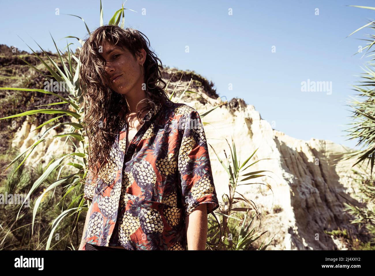 woman with curly wild hair at beach smiles by sandstone in Portugal