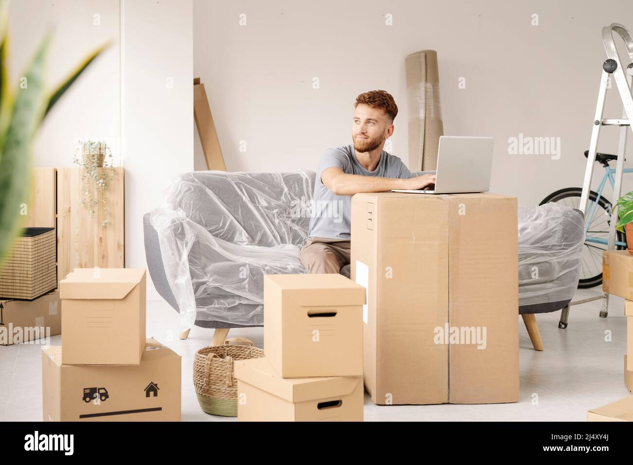 A young man resting from moving into his new home using his laptop. Stock Photo