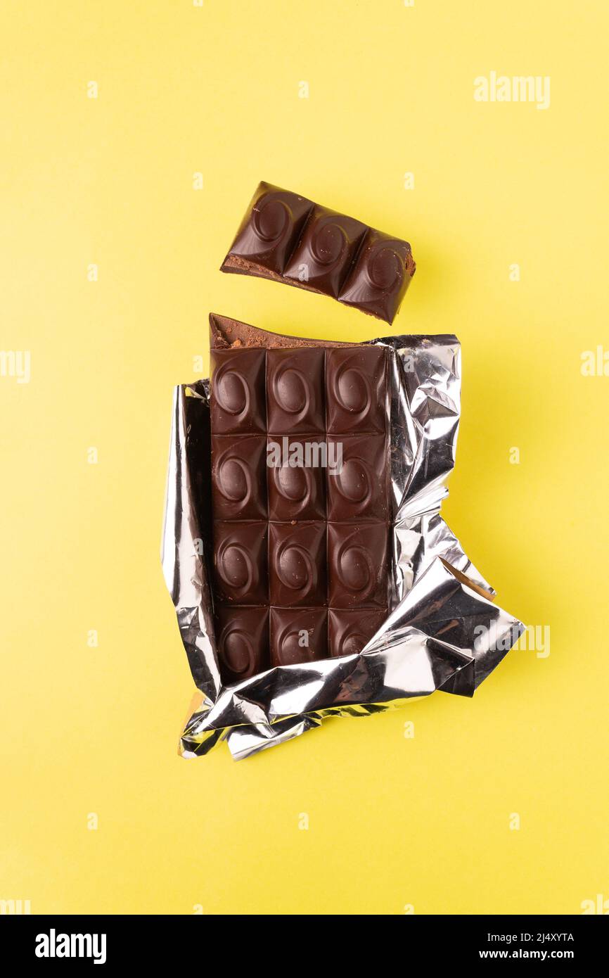 dark chocolate bar in a shiny wrapper on a yellow background Stock