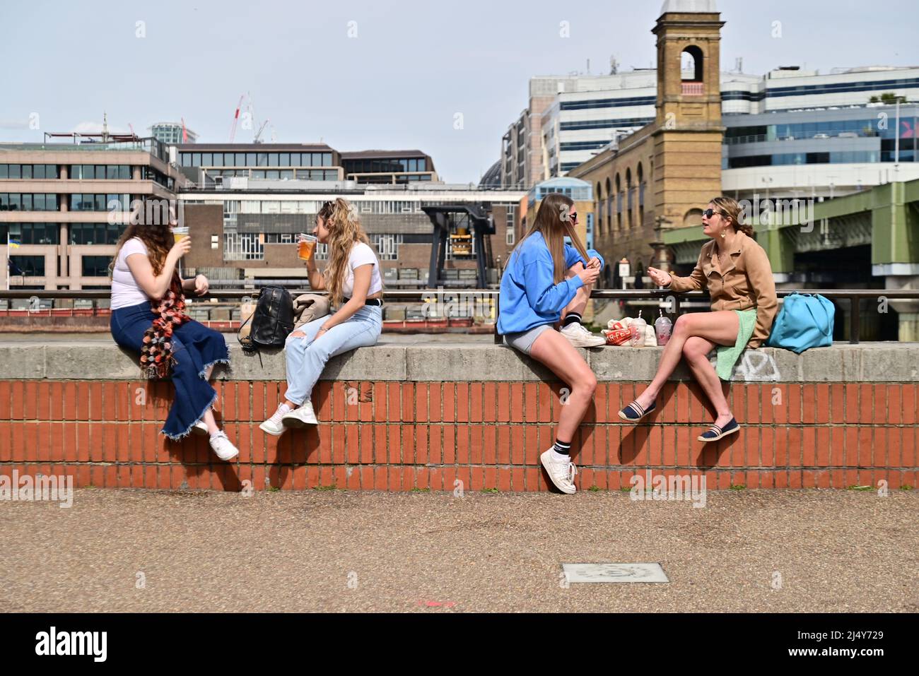 London, UK, Easter Monday, 18th April 2022, Weather. Warm sunshine on the bank holiday. Friends relax and talk while sitting on a wall on the south bank of The Thames. Credit: Paul Biggins/Alamy Live News Stock Photo