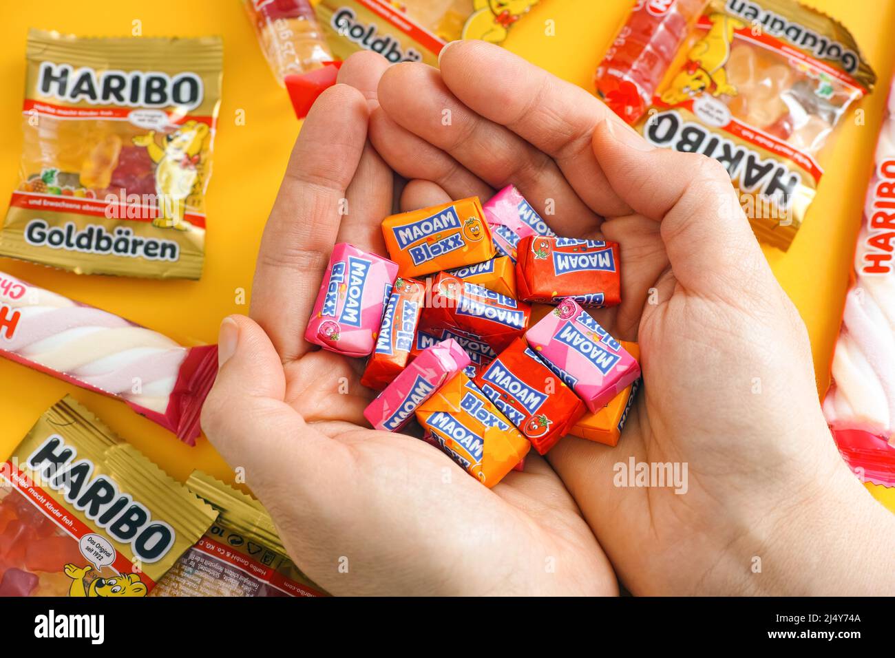Tambov, Russian Federation - January 06, 2021 Woman palms full of Maoam Bloxx candies. There are some Haribo candies on yellow background. Stock Photo