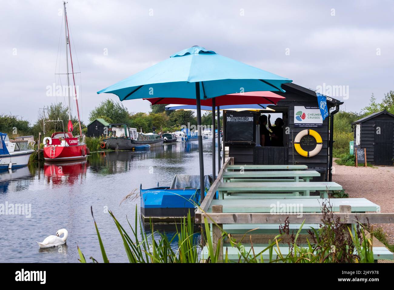 Couple in silhouette inside a kiosk. One appears to reach for something. Colourful umbrellas line the canal side and a white swan swims up and down. Stock Photo