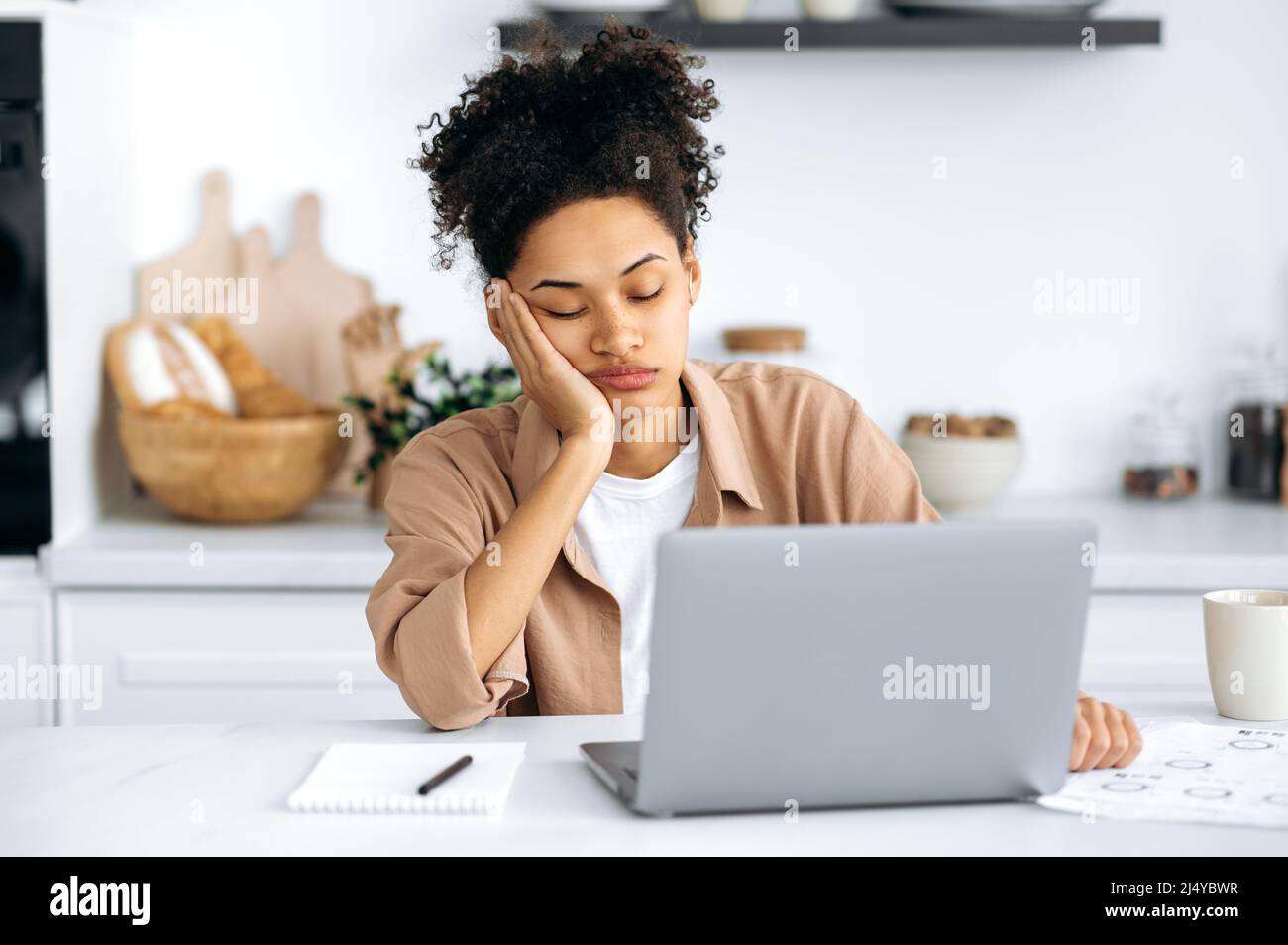 Exhausted african american girl with closed eyes, freelancer or student, working remotely from home, tired of boring online work, suffering from chronic fatigue, overwork, falls asleep at the desk Stock Photo