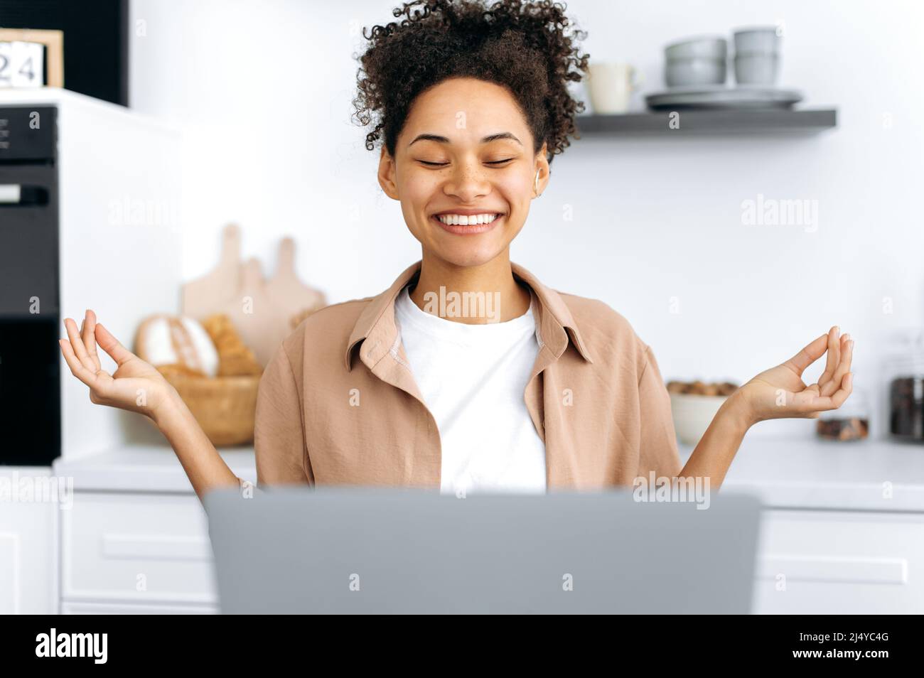 Pretty, happy african american girl resting during work. Positive female student or freelancer, sits at home in the kitchen, takes a break from online work or learning, eyes closed, meditate, relaxing Stock Photo