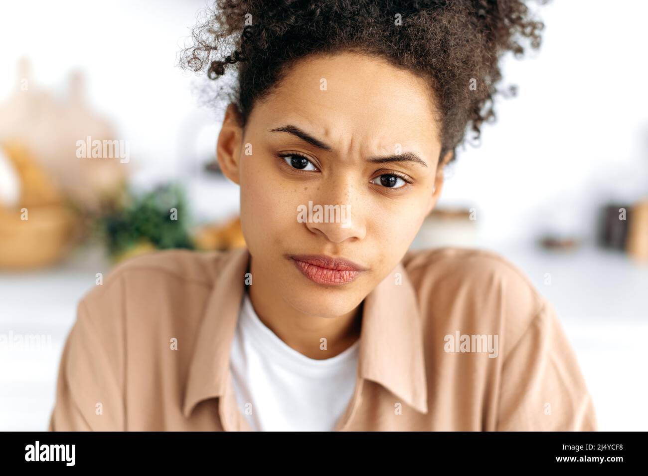 Close-up face of a frowning puzzled african american curly-haired millennial girl with freckles, knitted her eyebrows, looks unhappily at the camera, feels misunderstanding, anxiety Stock Photo