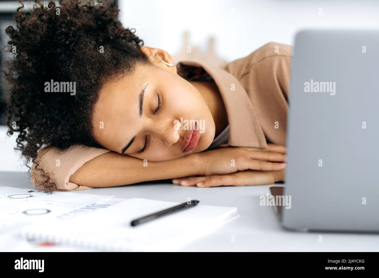 Close-up of a tired exhausted african american girl, female freelancer or student, fell asleep at the desktop near the laptop, overworked from working or studying online, needs rest and sleep Stock Photo