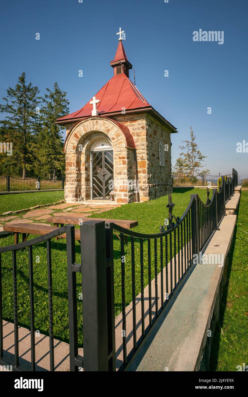 Small stone Christian chapel in remote mountain area with black metal fence in front on a beautiful day of summer. Stock Photo