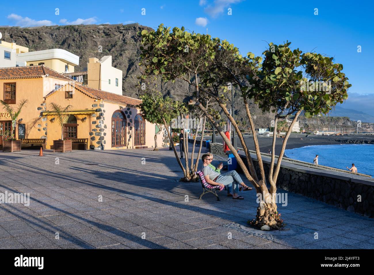 Tazacorte at La Palma Island Spain - March 07, 2022: Boulevard and couple sitting at wooden bench relaxing during sunset at Atlantic Coast Stock Photo