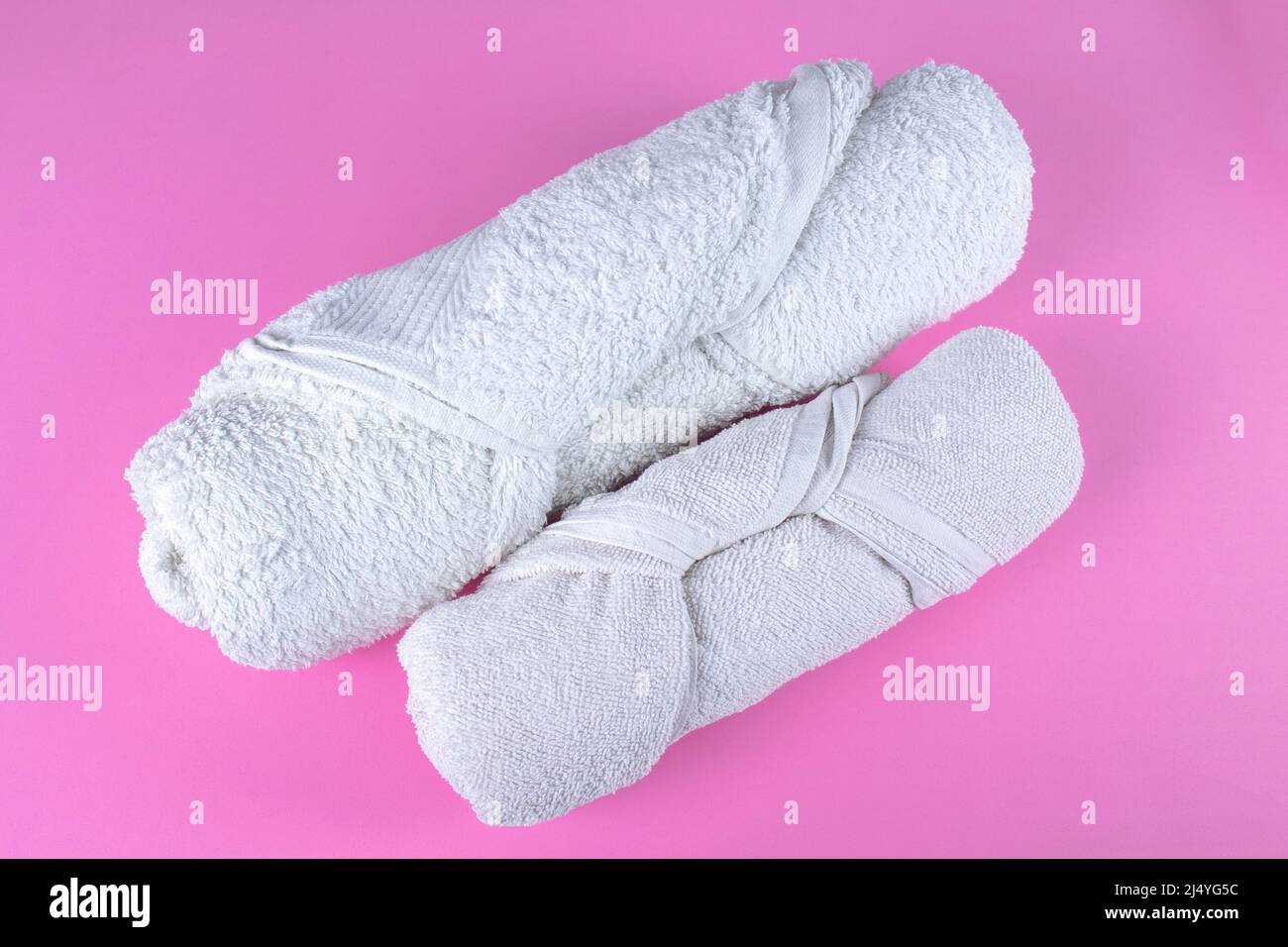 Two folded rolled white bathroom towels on pink background. Stock Photo