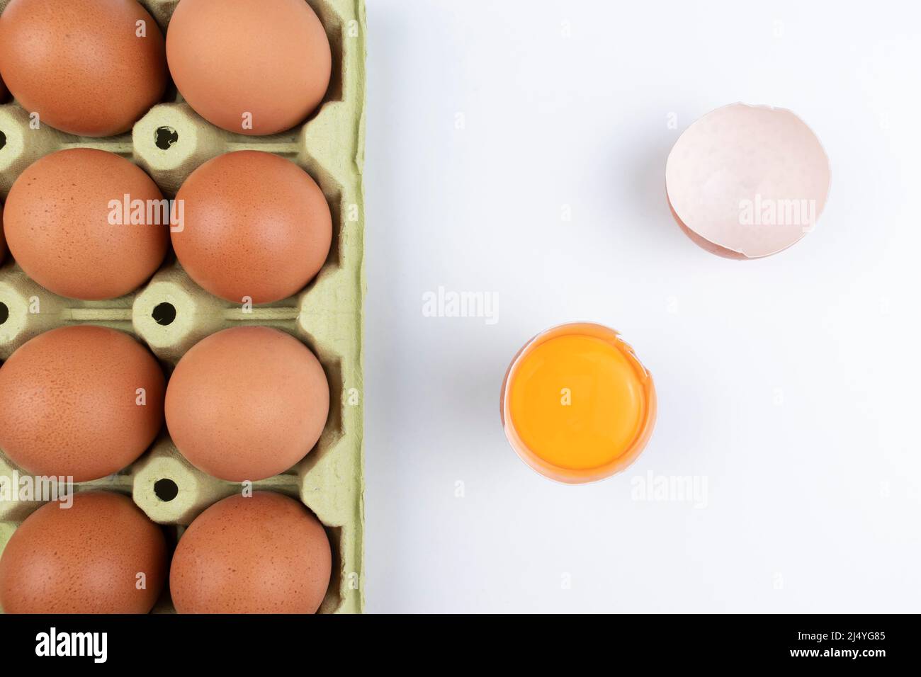 Pack of brown eggs with one broken open egg with raw yolk and shell on white background. Stock Photo